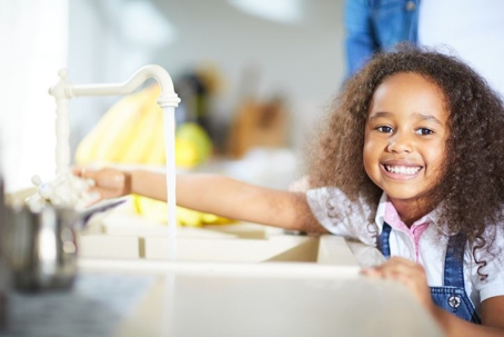 Little girl smiling as she turns on faucet
