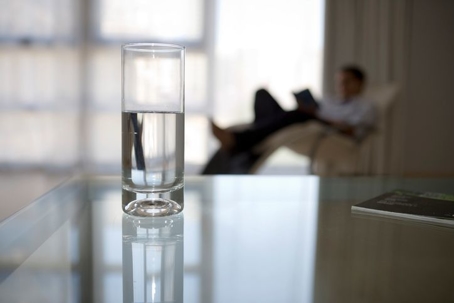 Glass of clean water and a man reading a book in the background