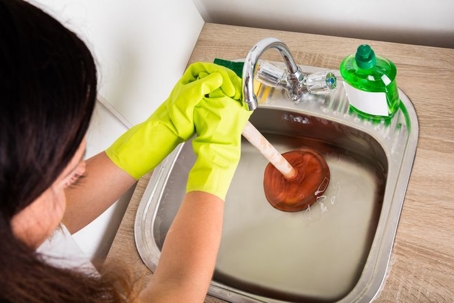 Woman using a plunger in the sink